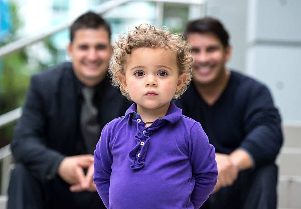 two years old little girl posing with two smiling adult men in the background