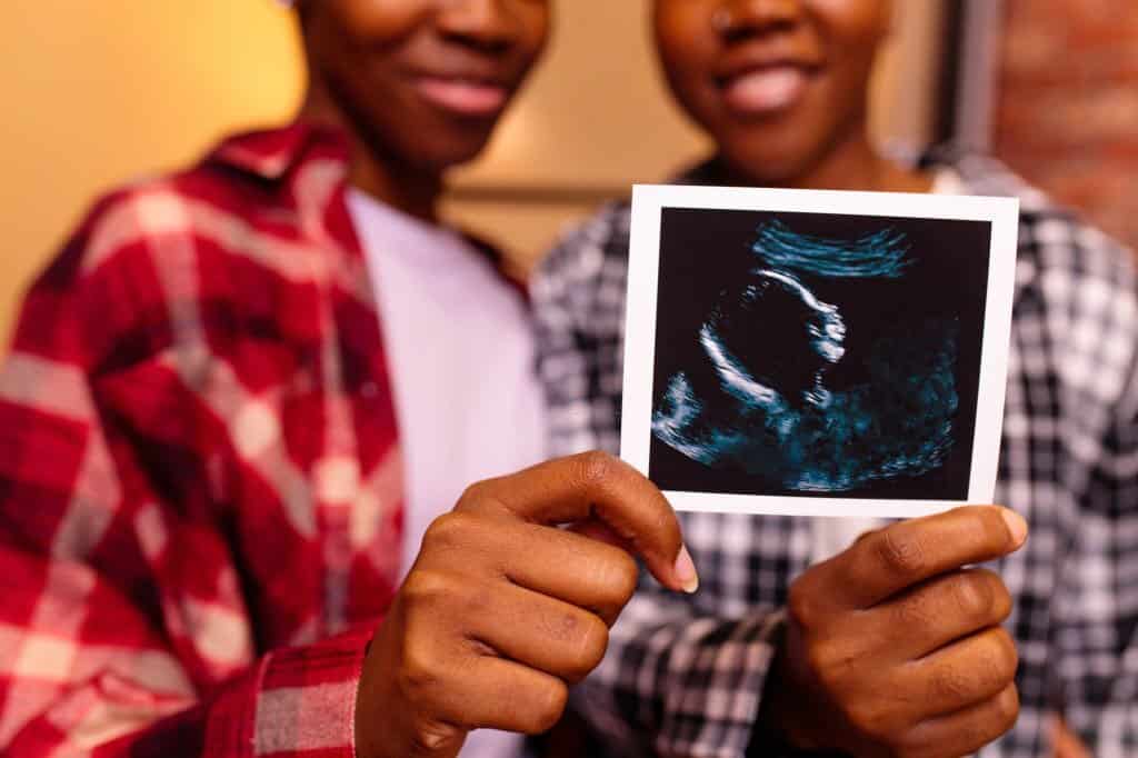 african american two happy future mothers sonogram image at home in evening.
